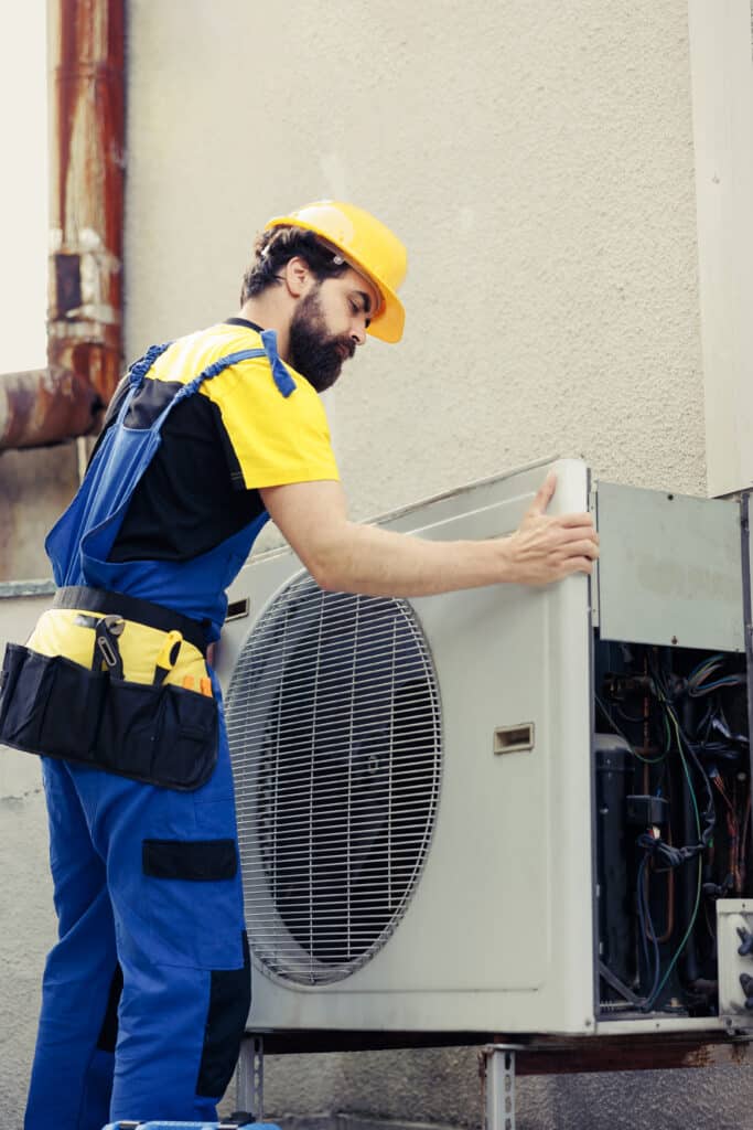 Servicing HVAC unit, HVAC technician repairing air conditioning system outside, HVAC repair, heating and cooling services, professional HVAC technician at work.