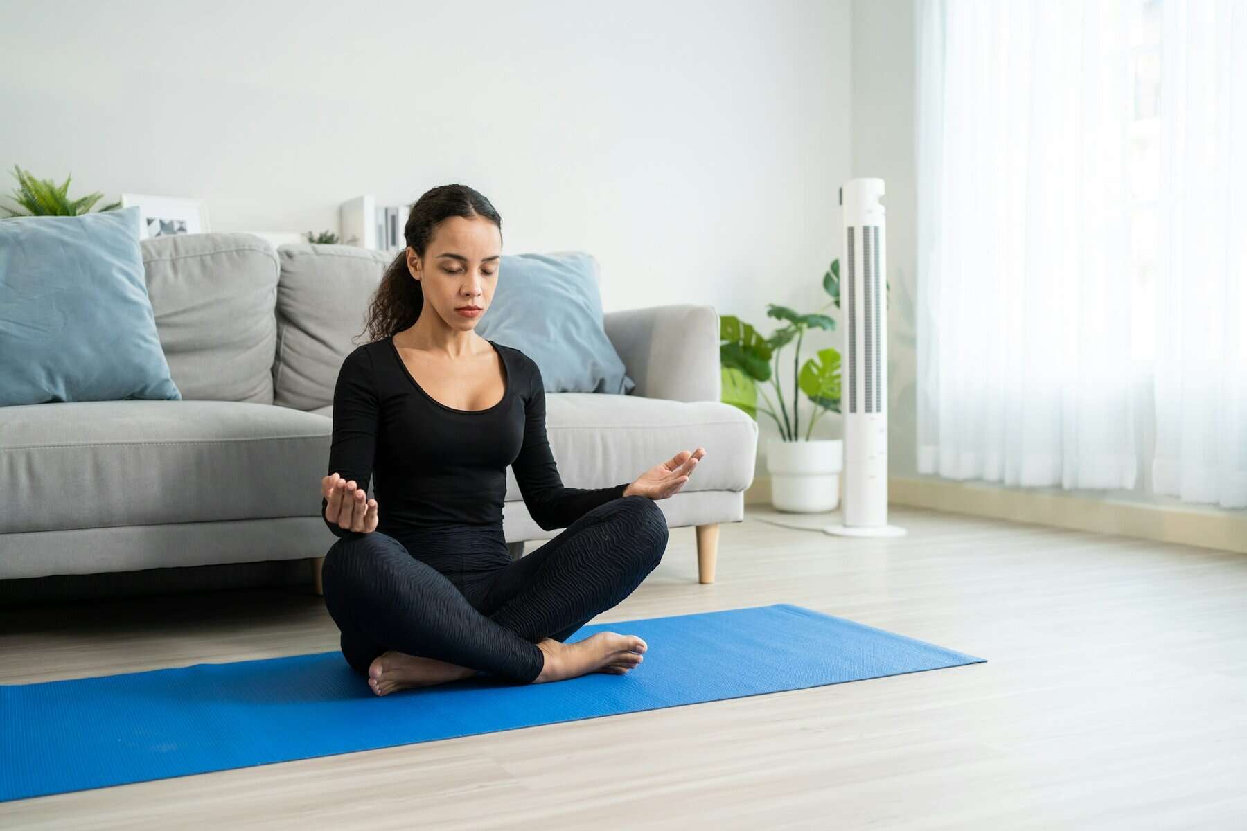 Relaxing woman meditating in living room for stress relief, healthy lifestyle, and mindfulness, with an air purifier in background.