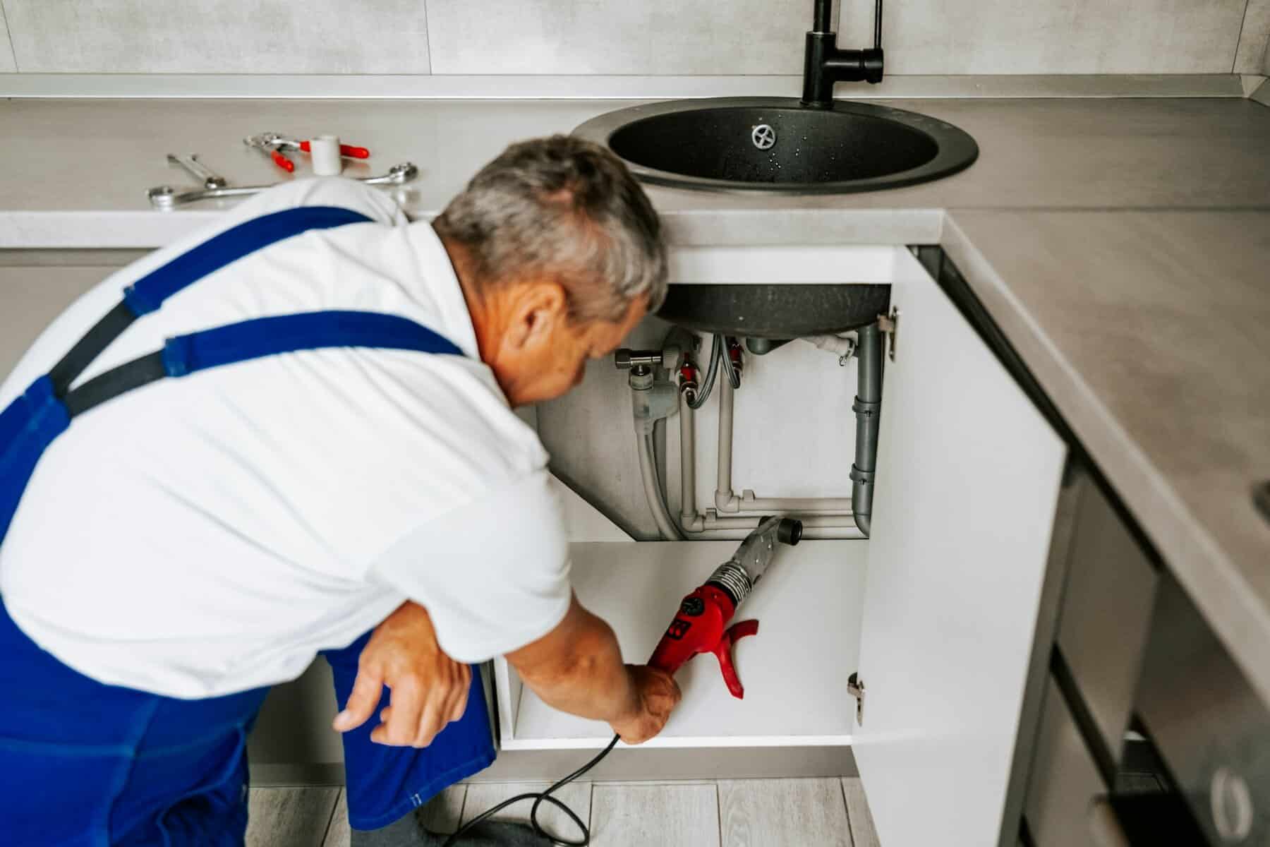 Efficient plumber repairing under-sink piping, showcasing professional HVAC and plumbing services, ensuring reliable home maintenance and leak prevention.